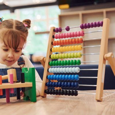 Cheerful little girl in casual clothes playing in kindergarten with toys.